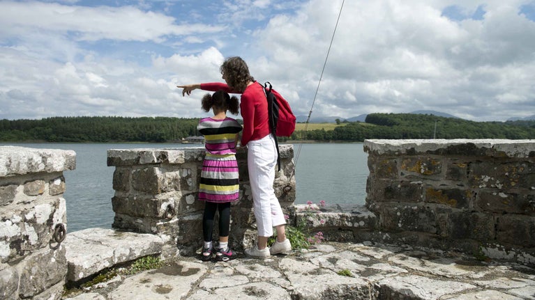 Woman and child enjoying the view from the battlements at Plas Newydd Country House and Gardens, overlooking the Menai Strait and views of Snowdonia.